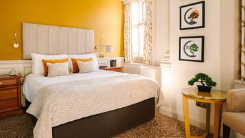 A hotel room with a bed, bedside table, lamp, and a small table with a plant.