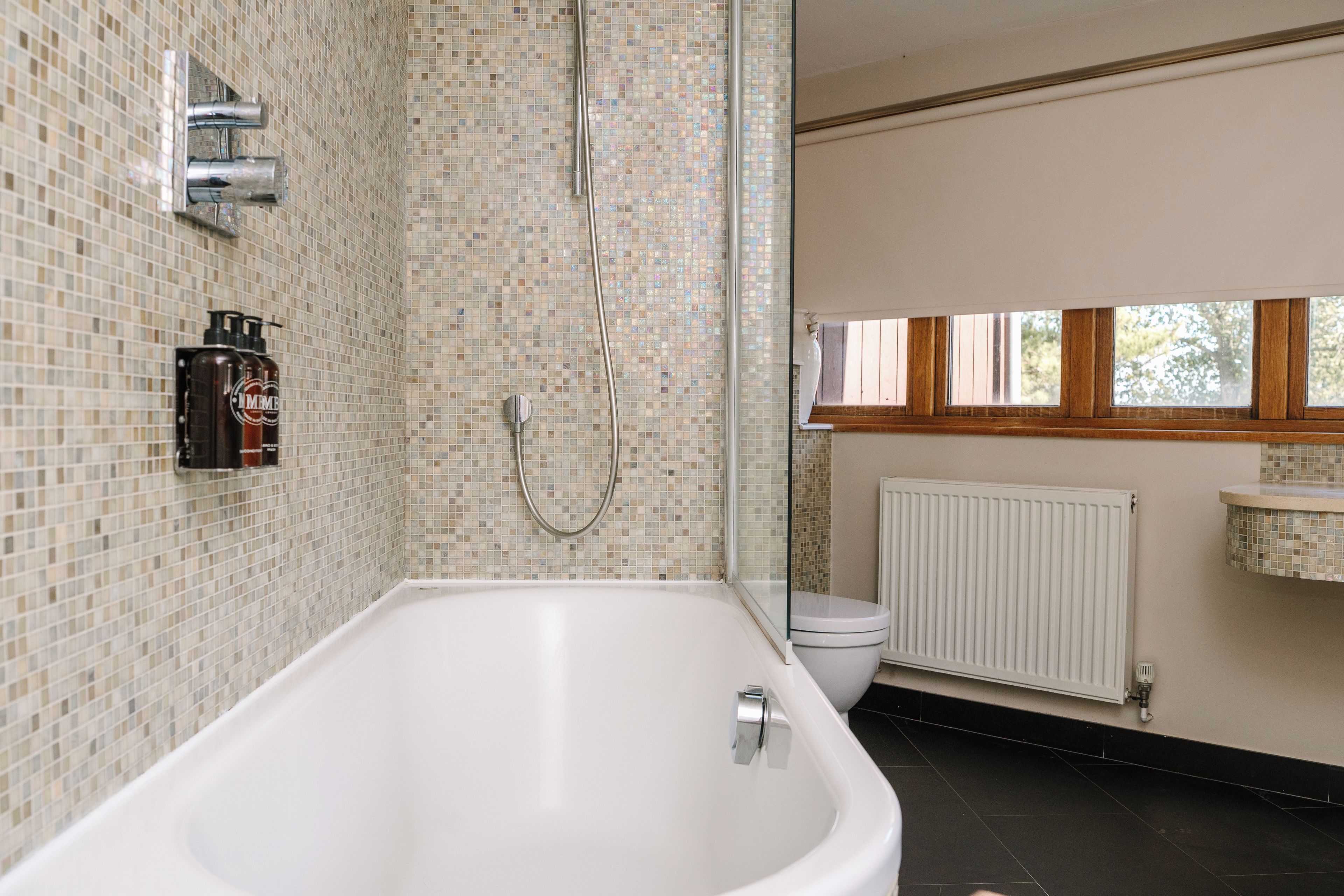 A bathroom with a bathtub, shower, toilet, and a window.
