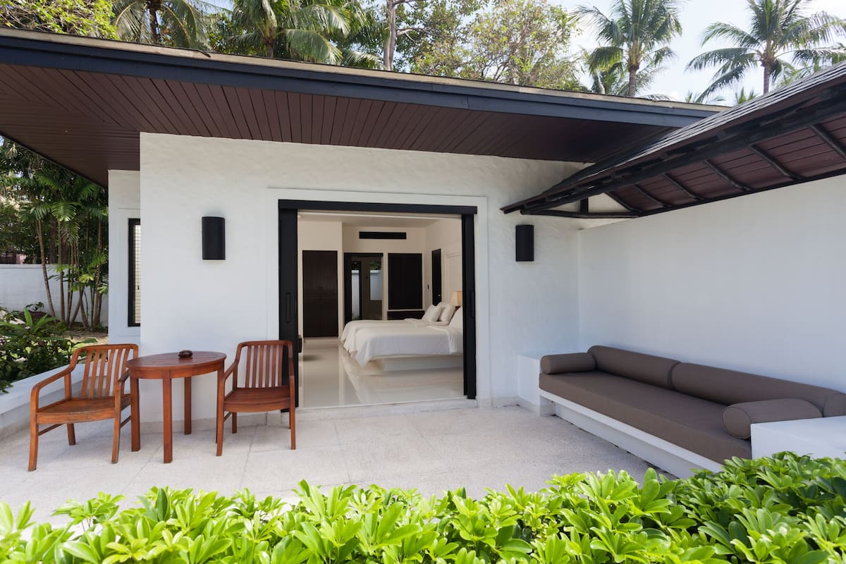 A modern outdoor seating area with a sofa and chairs, a small table, and a doorway leading to a bedroom.
