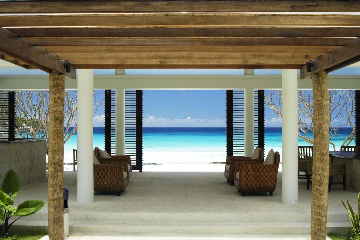 A covered outdoor seating area with wicker furniture and a view of a beach.