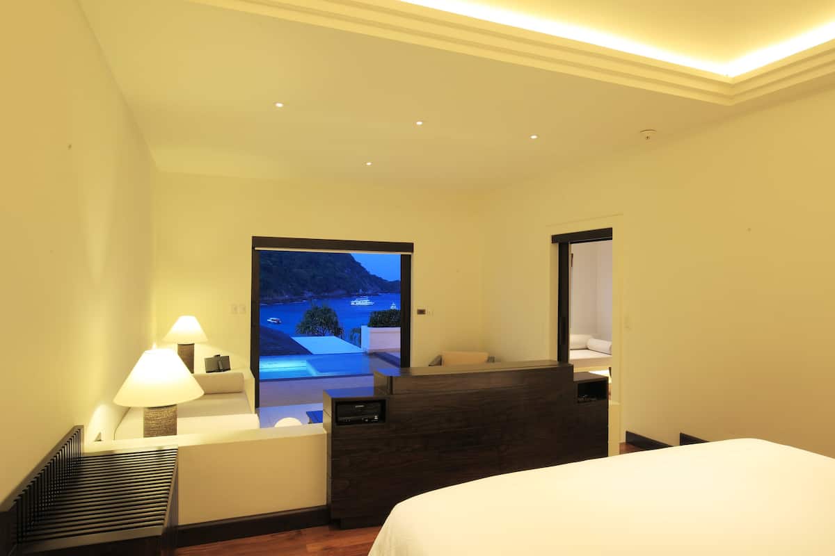 A hotel room with a bed, a desk, a chair, and a view of a mountainous landscape through a large window.