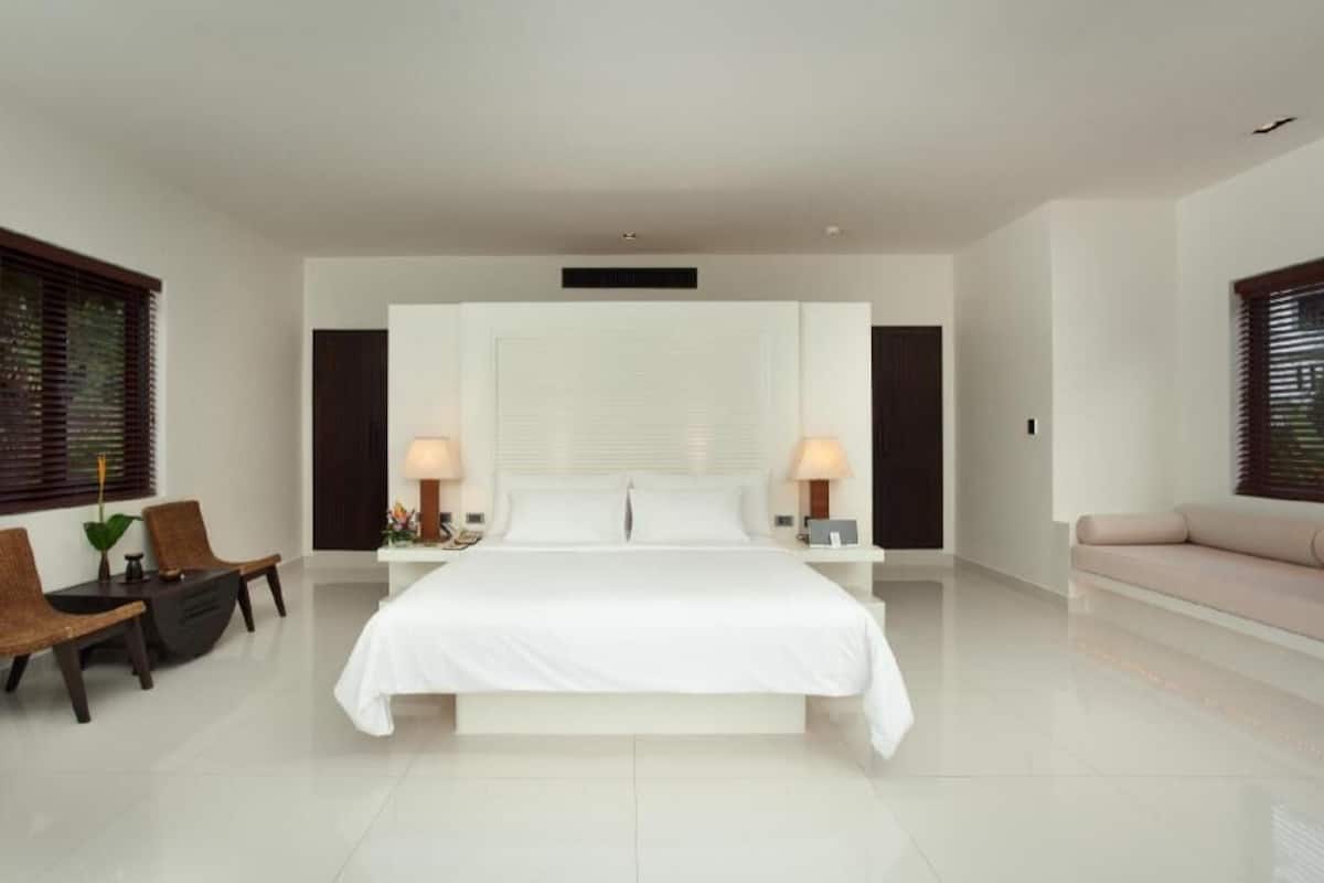 A modern bedroom with a large bed, two bedside tables with lamps, a sofa, and a seating area with chairs.