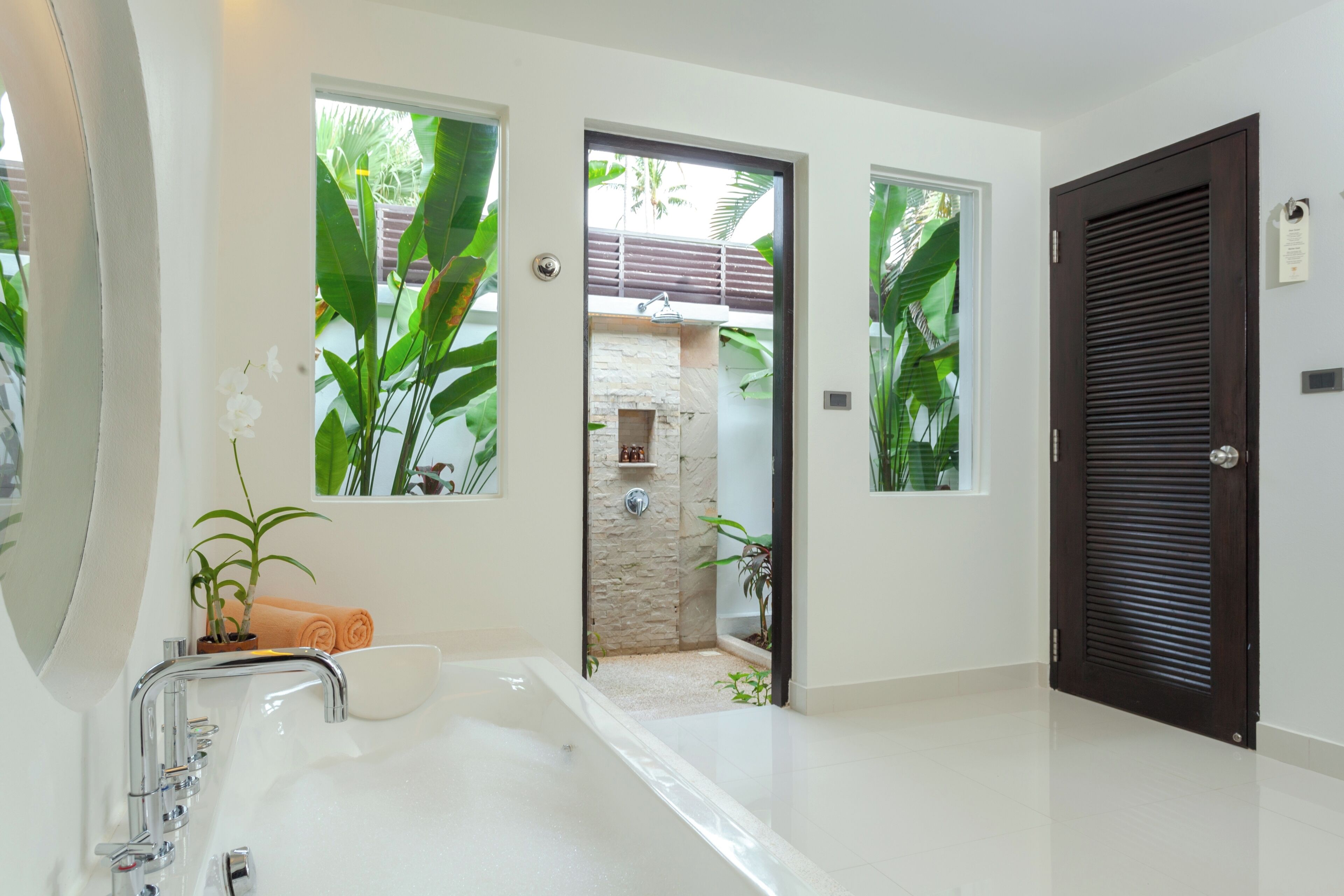A modern bathroom with a large bathtub, a shower, and a door leading to an outdoor area.