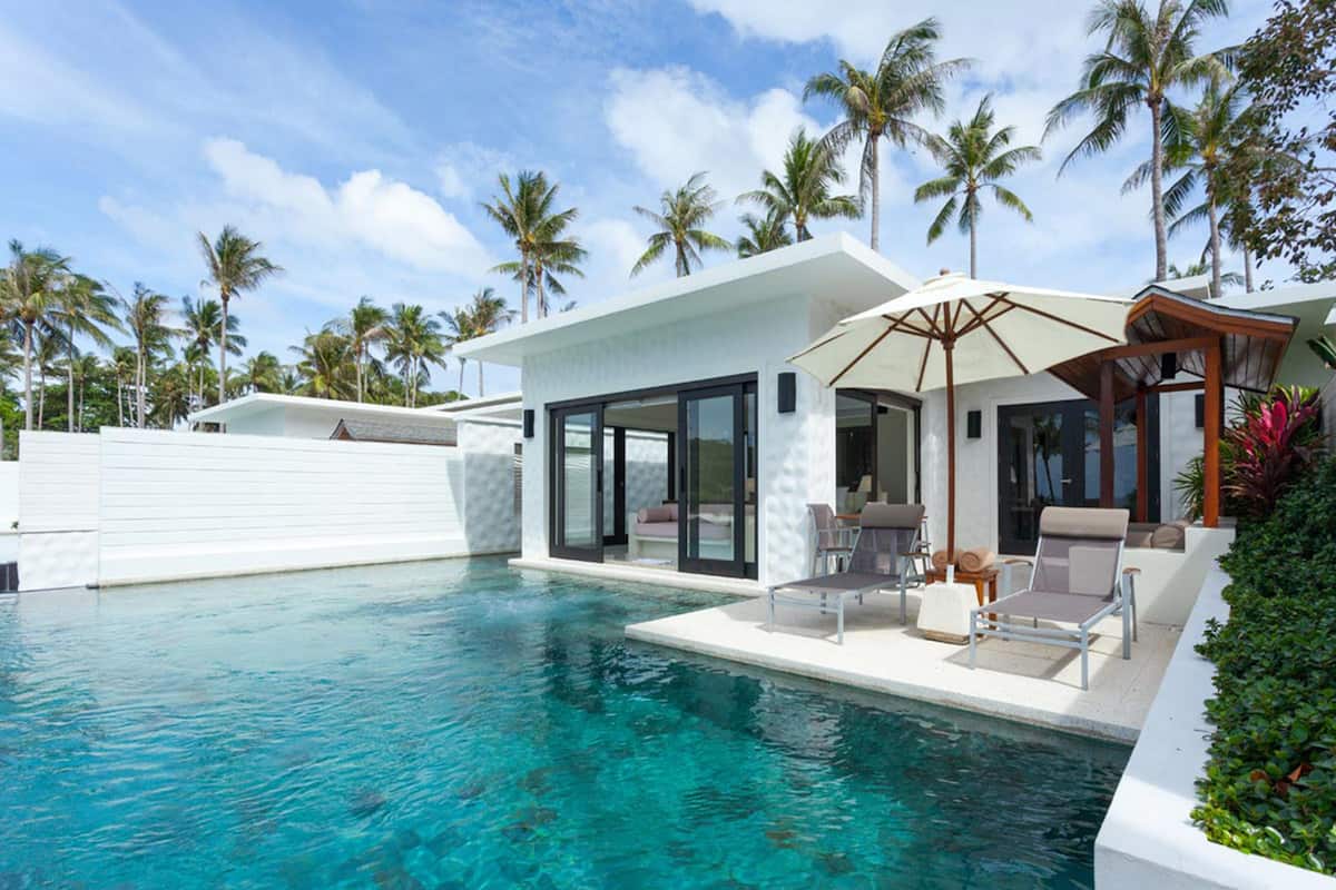 A modern poolside area with a clear pool, lounge chairs, and a covered seating area.