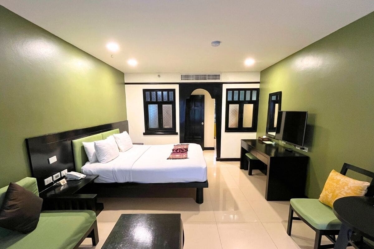A hotel room with a bed, a desk, a TV, a sofa, and a chair.