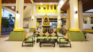 Un vestíbulo espacioso con decoración verde y amarilla, que presenta una zona de estar central con una mesa de café y varias sillas.