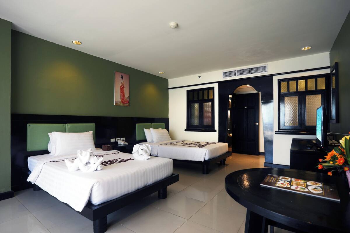 A hotel room with two beds, a dining table, and a painting on the wall.