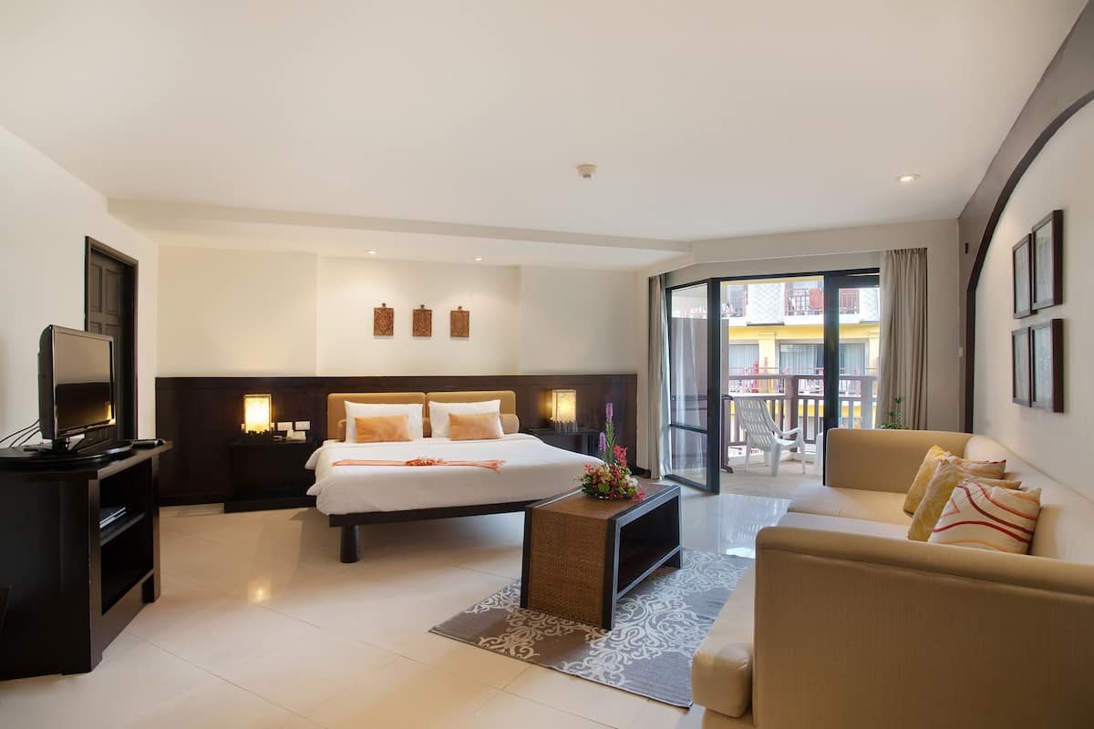 A modern hotel room with a bed, a sofa, a TV, a coffee table, and a balcony with a view.