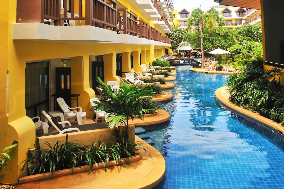 A hotel with a swimming pool, lounge chairs, and a covered area with umbrellas.