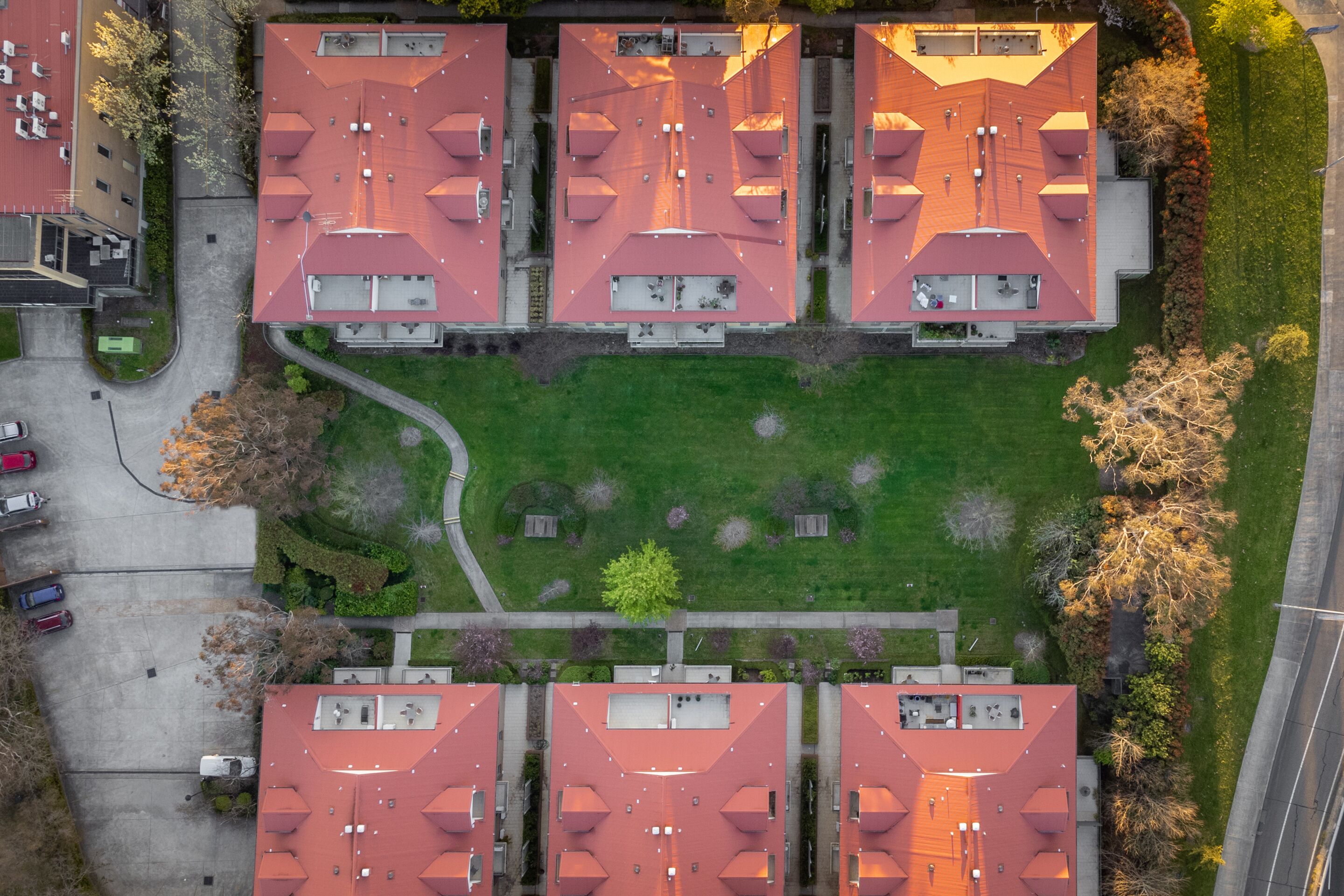 An aerial view of a residential complex with four red-roofed buildings, a central green lawn, and surrounding trees.