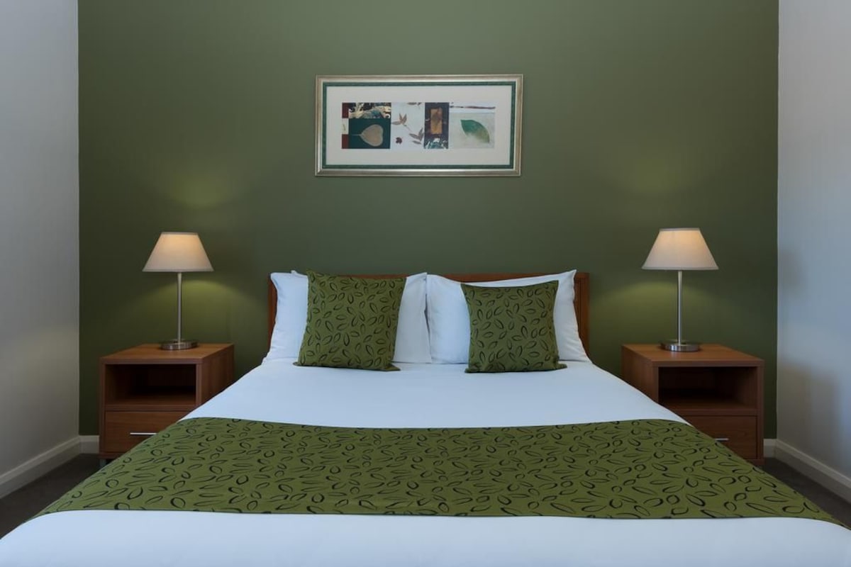 A neatly made bed with a green patterned bedspread, two matching pillows, and two bedside lamps on wooden nightstands.