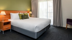 Una habitación de hotel con una cama grande, dos mesitas de noche, una silla y un ventanal con cortinas.