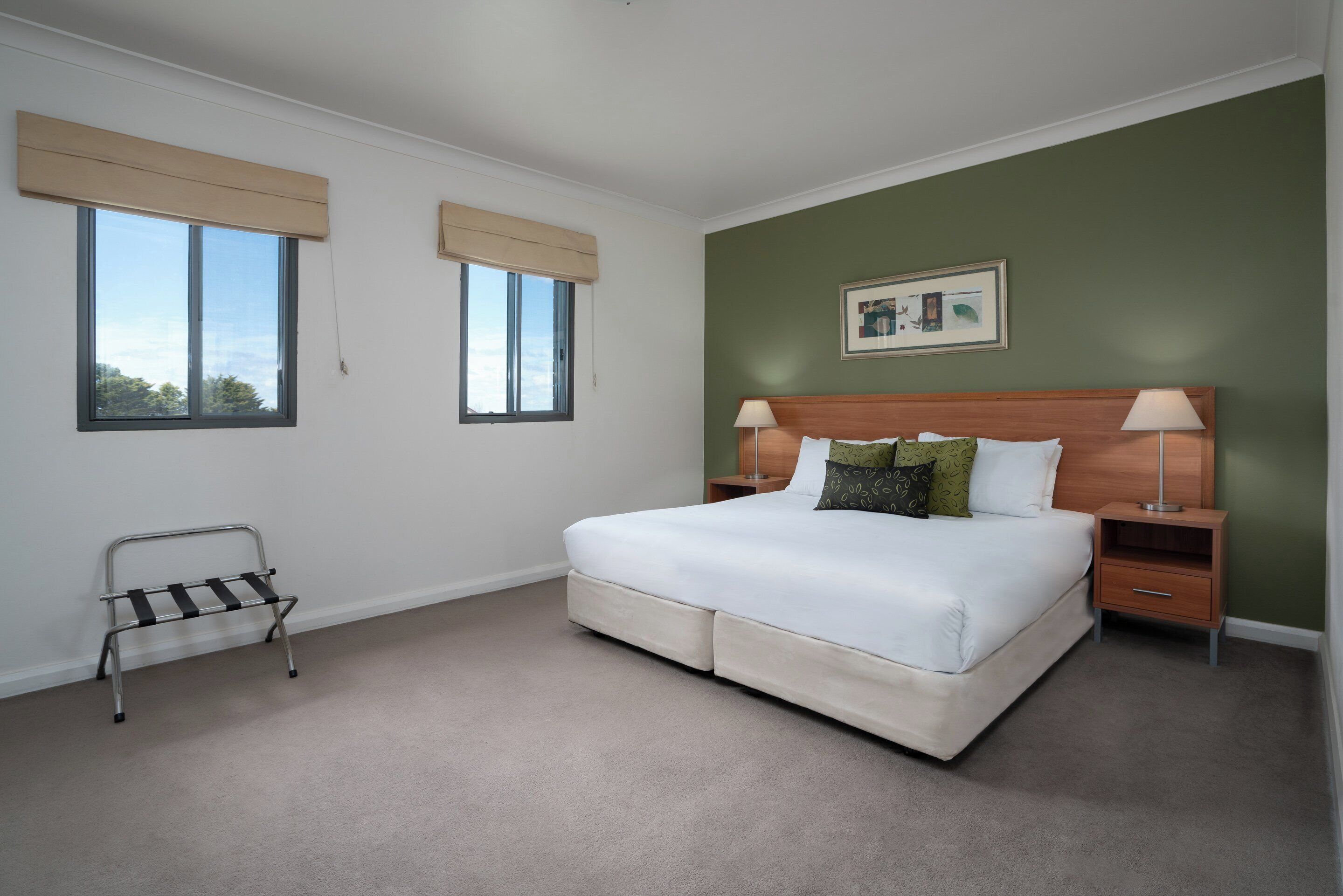 A bedroom with a bed, bedside tables, a nightstand, a window with a blind, and a picture on the wall.