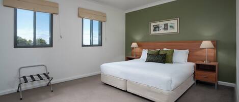 A bedroom with a bed, bedside tables, a nightstand, a window with a blind, and a picture on the wall.