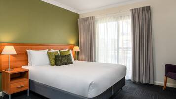 Una habitación de hotel con una cama grande, dos mesitas de noche con lámparas, una silla y una ventana con cortinas.