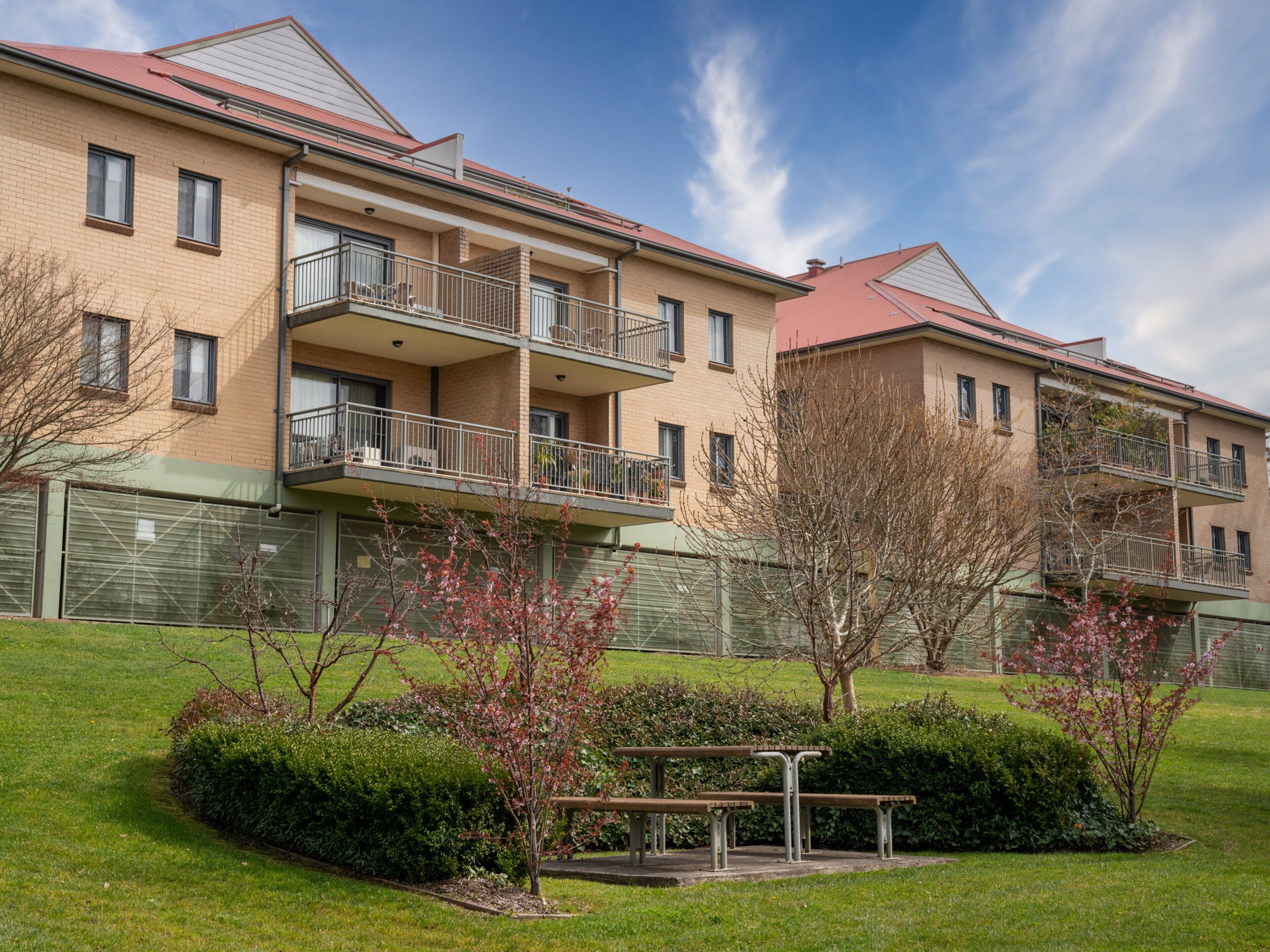A multi-story apartment building with balconies, a green lawn, and a picnic table.