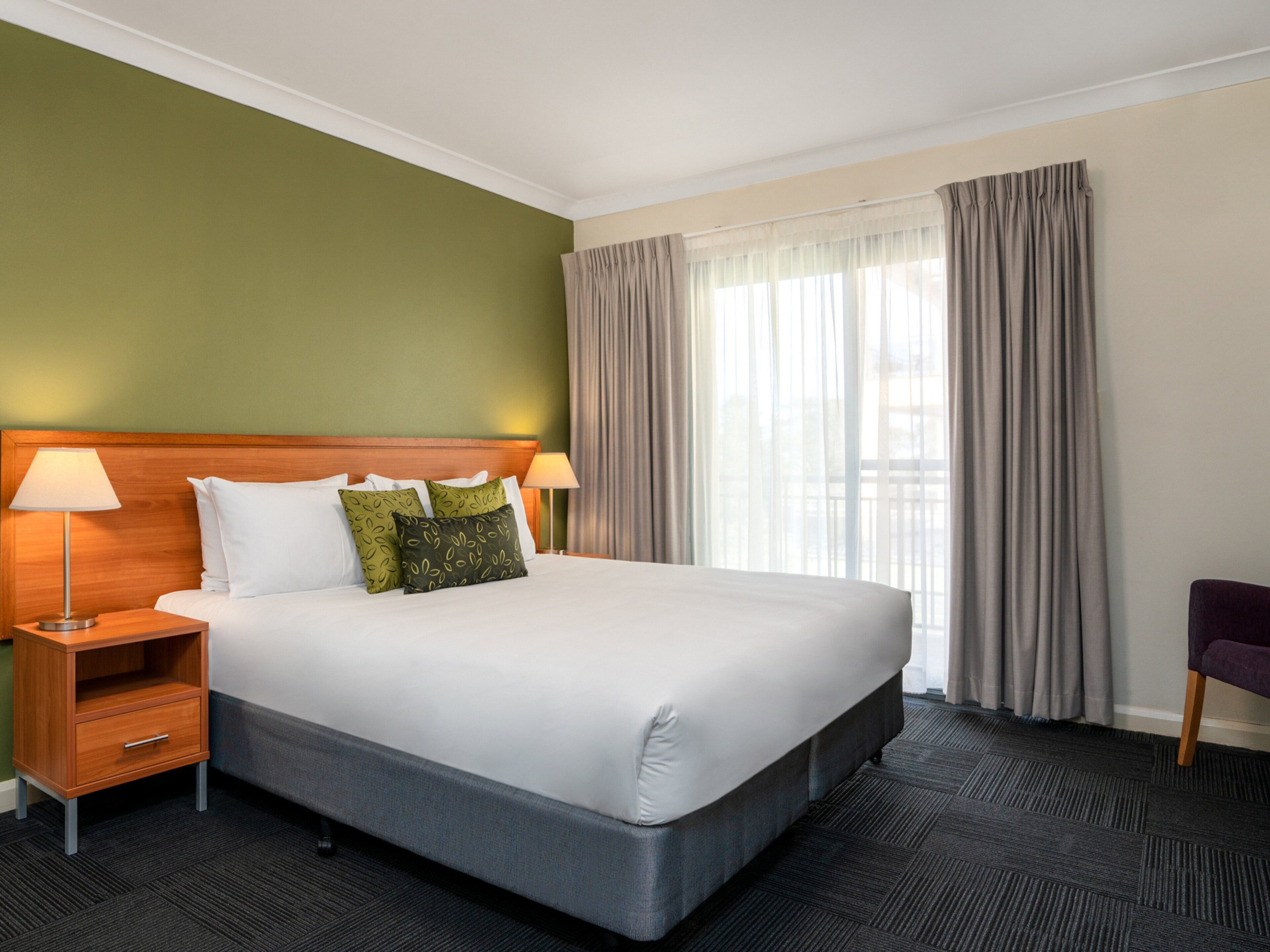 A hotel room with a large bed, two bedside tables, a nightstand, a chair, and a window with curtains.