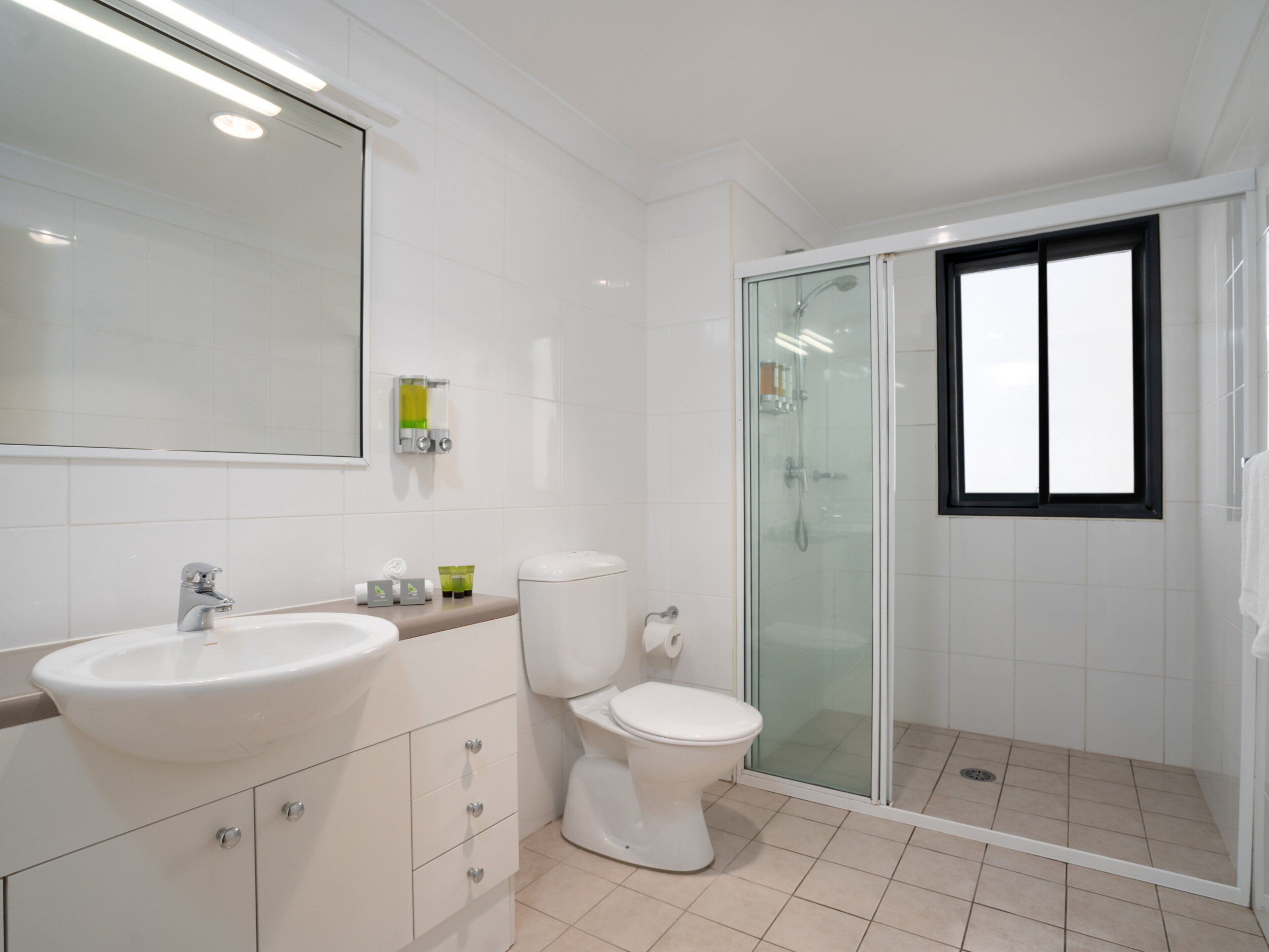 Un baño moderno con lavamanos blanco, inodoro y cabina de ducha con mampara de vidrio.