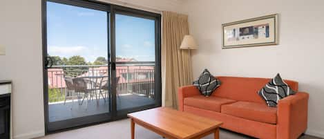Ein Wohnzimmer mit einer Couch, einem Tisch, einer Glasschiebetür zu einem Balkon und einem gerahmten Bild an der Wand.