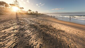 A beach with footprints, a clear sky, and buildings in the background.