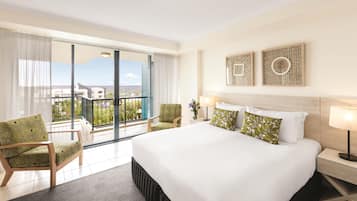 Et hotelværelse med en stor seng, et siddeområde med stole, en balkon med udsigt og to billeder hængende på væggen.