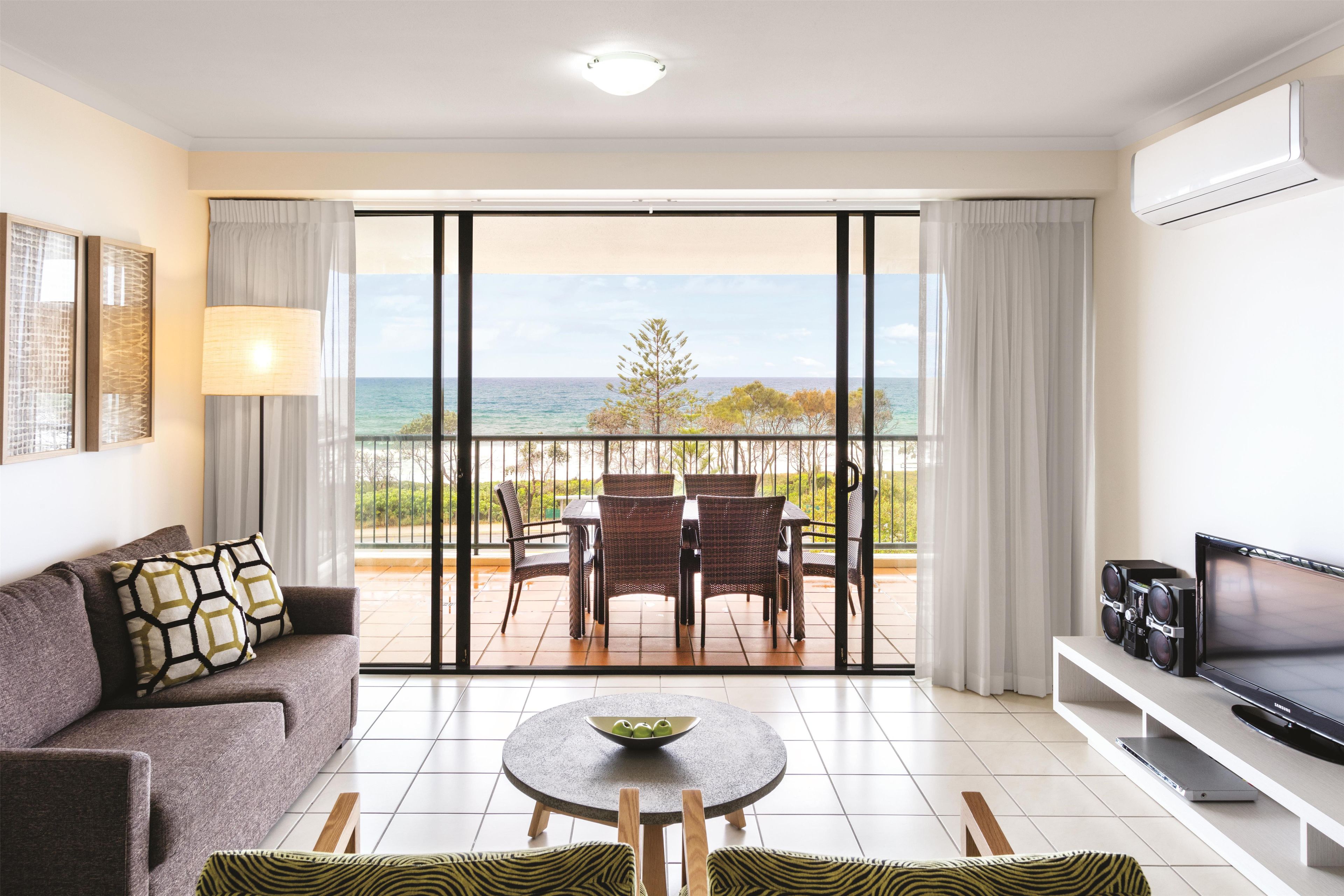 Un salón moderno con sofá, una mesa de centro, televisor y un balcón con vistas al mar.