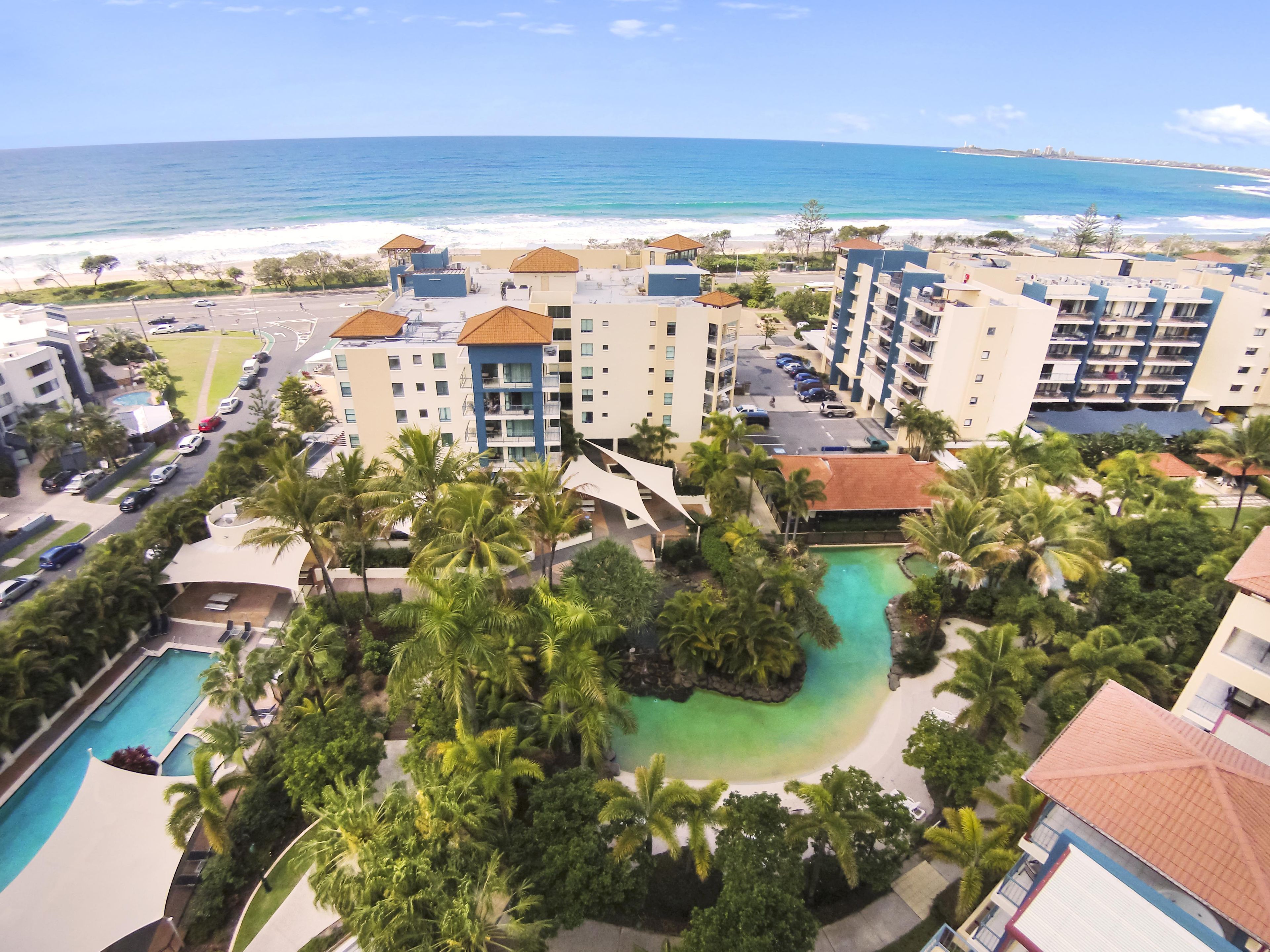 A resort with a pool, palm trees, and a view of the ocean.