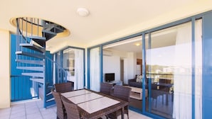 A modern interior with a spiral staircase, a dining area with wicker furniture, and a view through glass doors to a living space.
