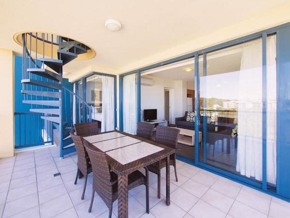 A modern interior with a spiral staircase, a dining area with wicker furniture, and a view through glass doors to a living space.