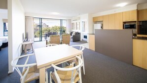 A modern hotel room with a dining area, kitchen, and a balcony with a view.