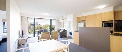 A modern hotel room with a dining area, kitchen, and a balcony with a view.