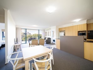 A modern hotel room with a dining area, kitchen, and a balcony with a view.