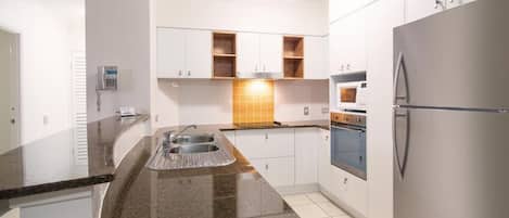 A kitchen with white cabinets, a granite countertop, a stainless steel refrigerator, and a built-in oven.