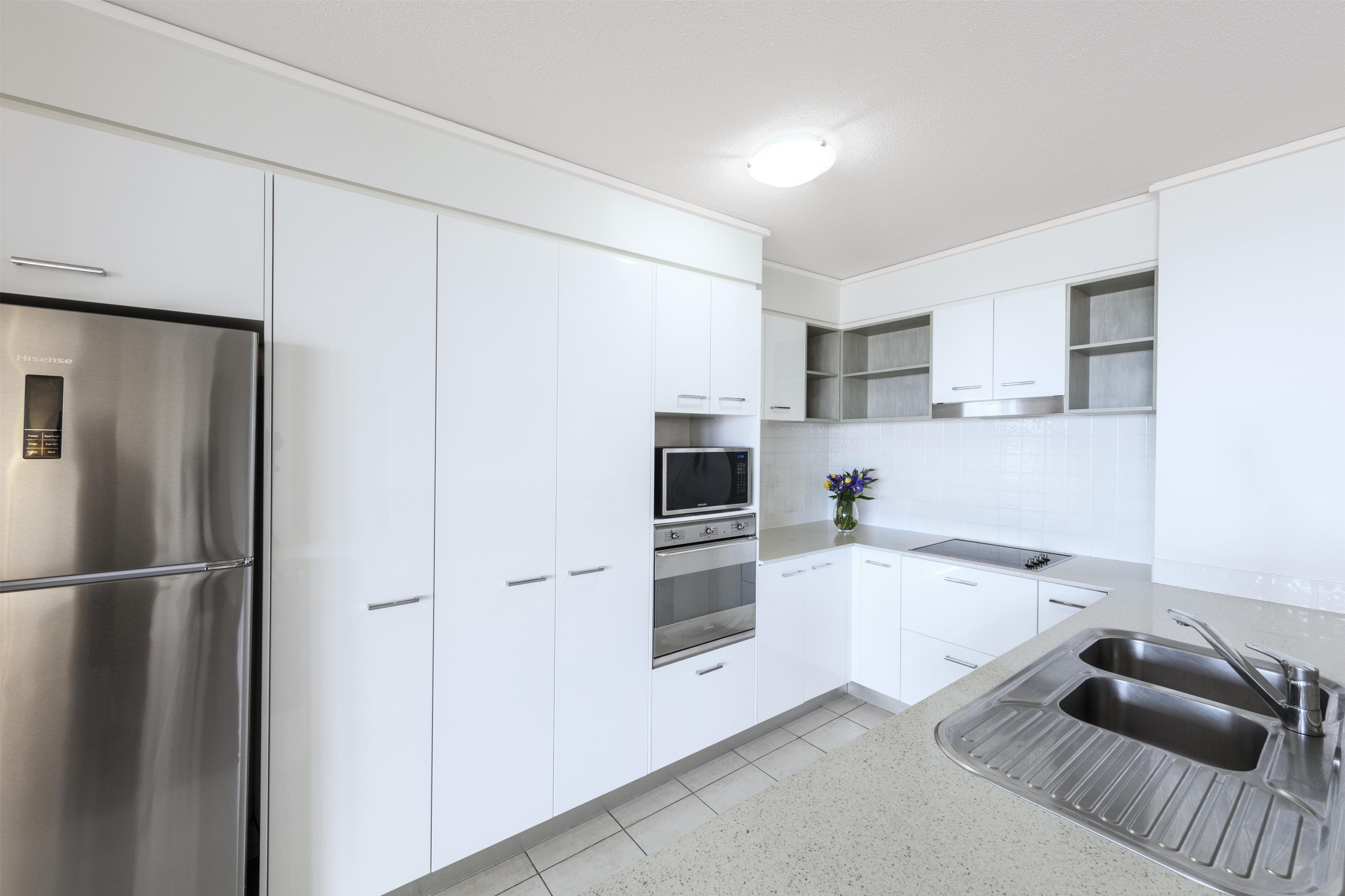 Una cocina moderna con armarios blancos, electrodomésticos de acero inoxidable y un microondas empotrado.
