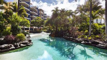 A resort pool with clear water, surrounded by tropical vegetation and a multi-story building.