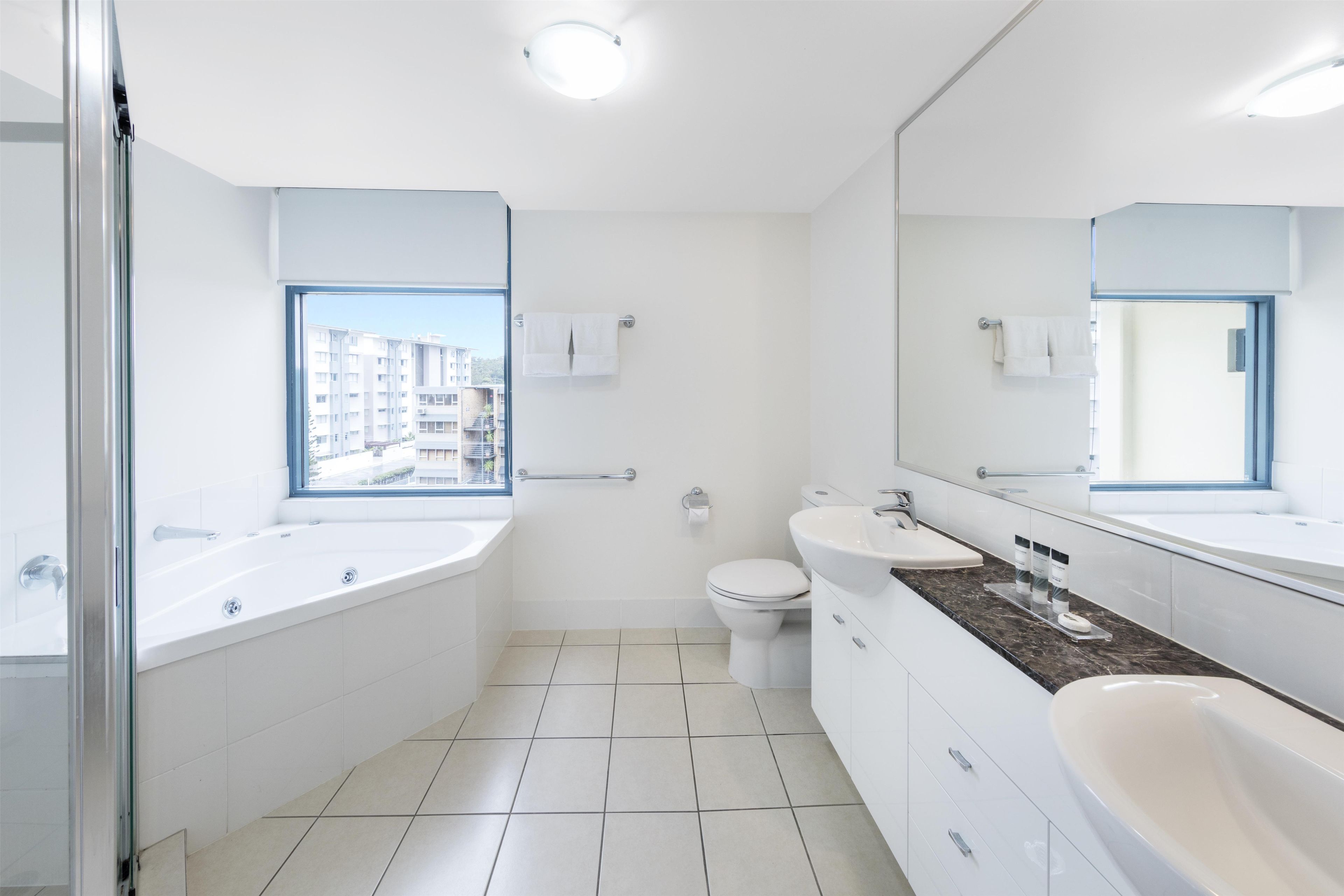 A modern bathroom with a large window, a bathtub, a toilet, and a sink.