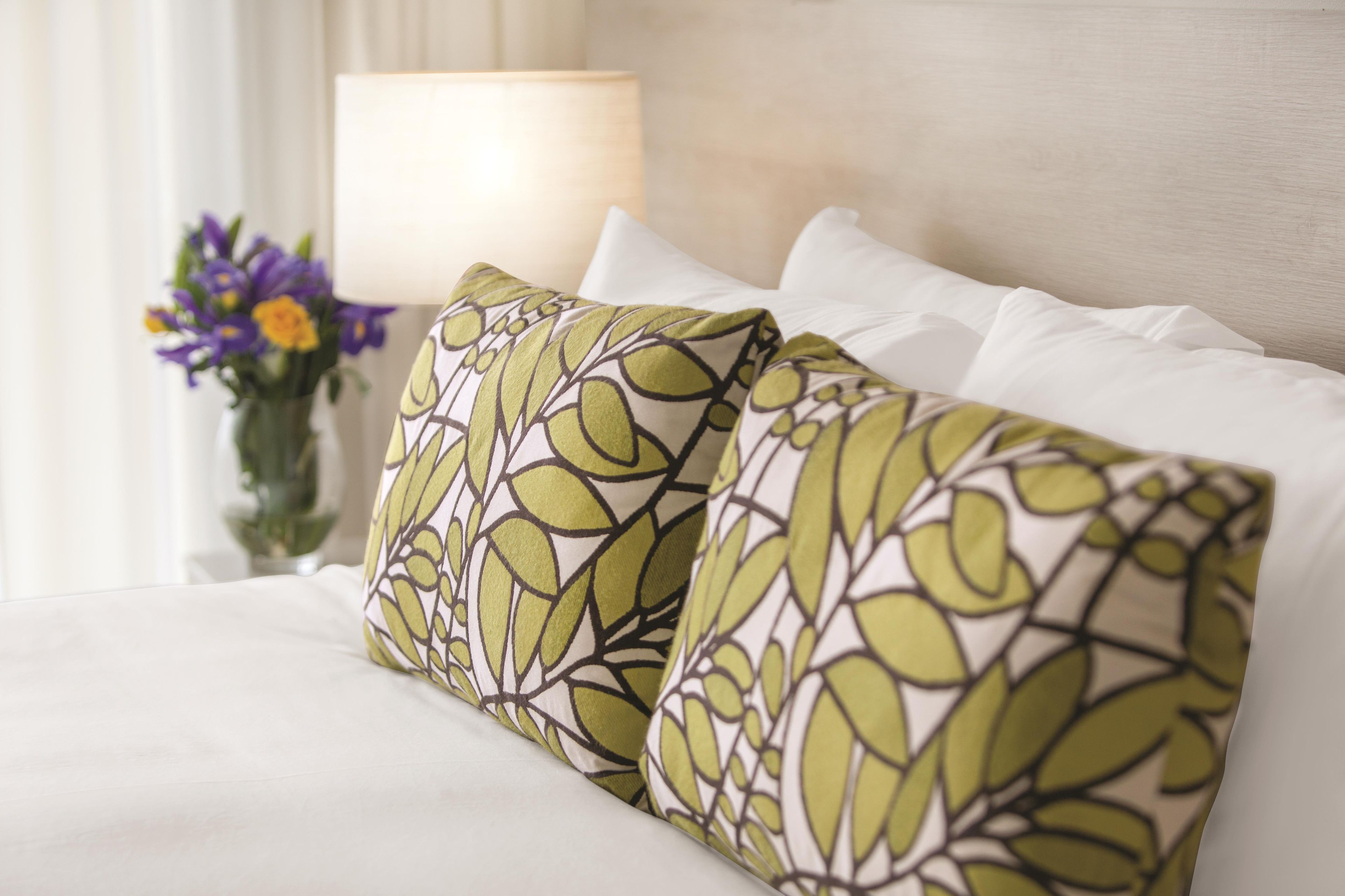 A bed with white bedding and two decorative pillows with a leaf pattern.