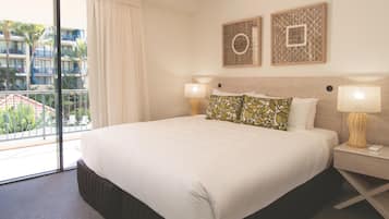 A hotel room with a large bed, two bedside lamps, a view of a building with balconies, and two framed wall art pieces.