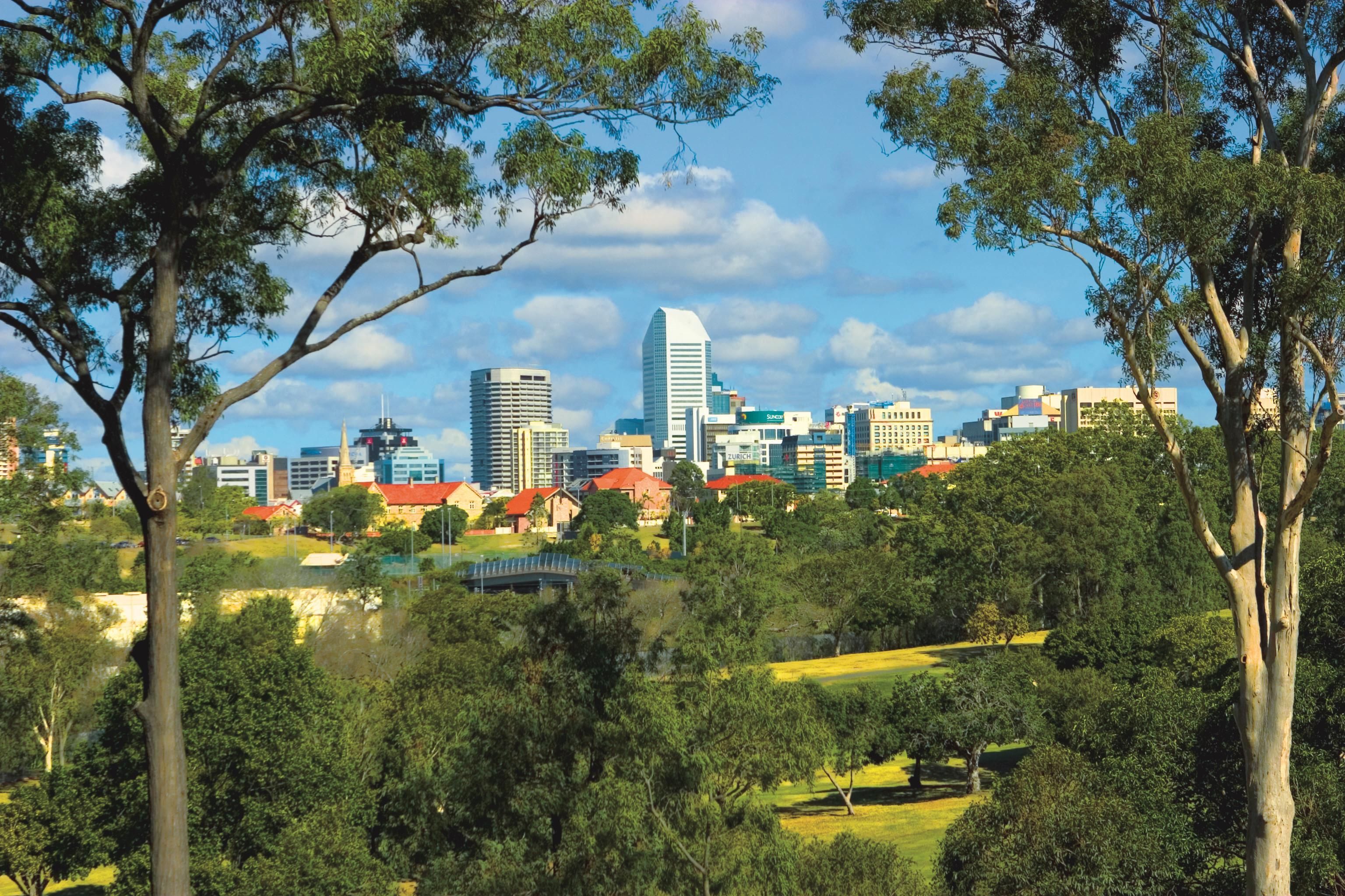 A city skyline with modern buildings, surrounded by green parks and trees.