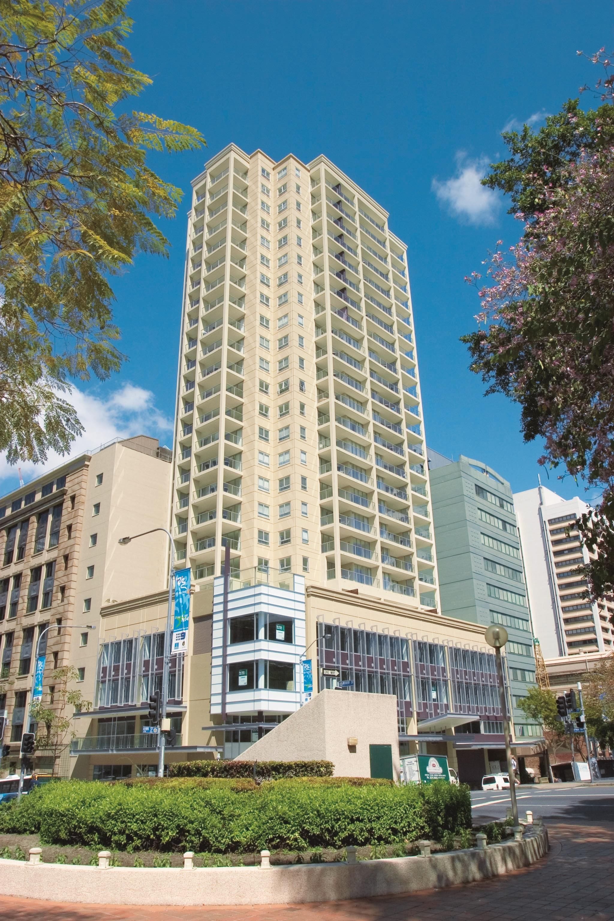 A high-rise building with multiple balconies, surrounded by other buildings and greenery.