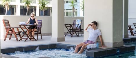 A pool area with a hot tub, lounge chairs, and a seating area with tables and chairs.