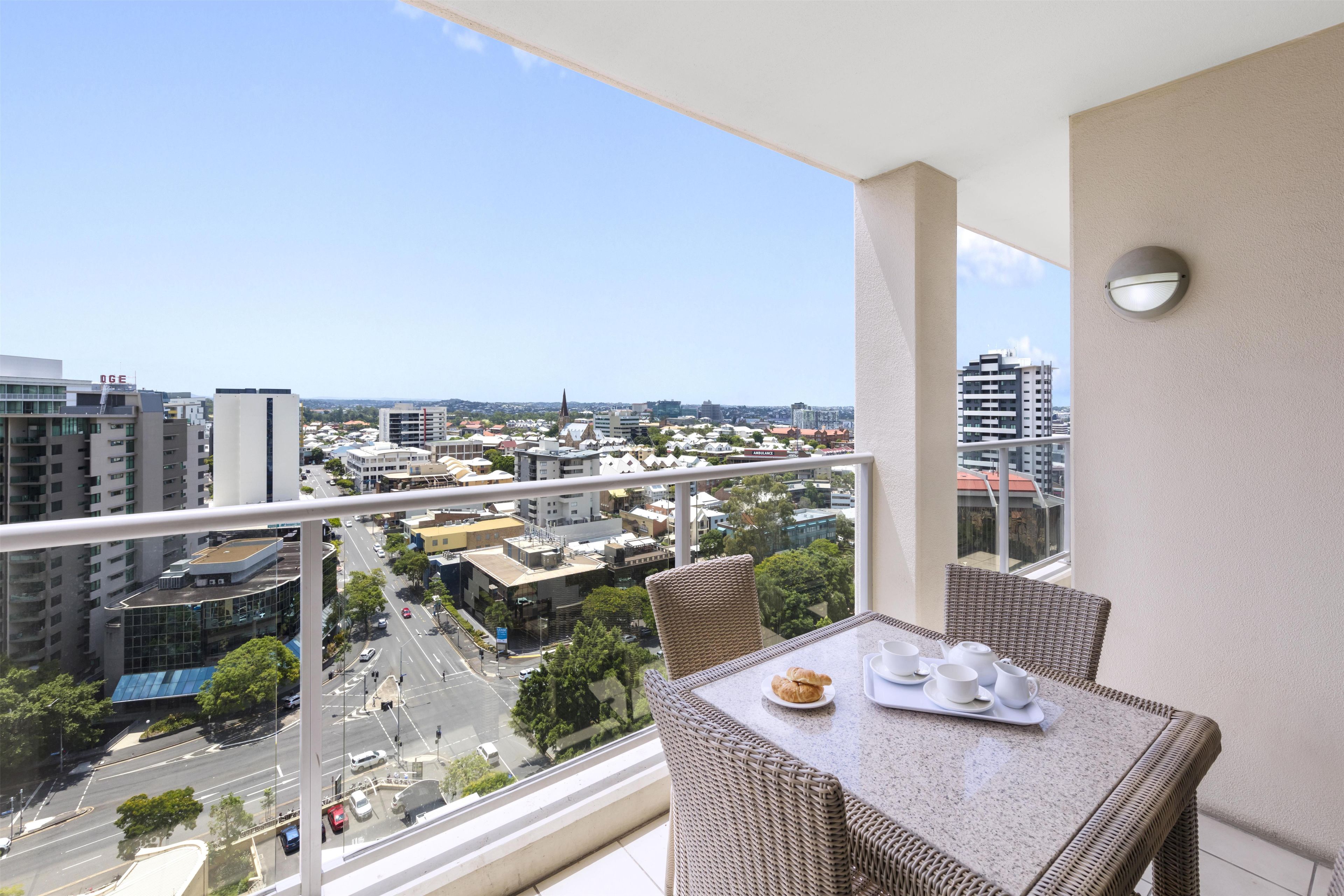 A balcony with a table set for two, overlooking a cityscape with buildings and a clear sky.