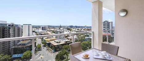 A balcony with a table set for two, overlooking a cityscape with buildings and a clear sky.