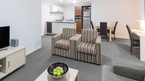 Een gezellige, compacte leefruimte met een bank, eethoek, kitchenette en een televisie op een standaard.