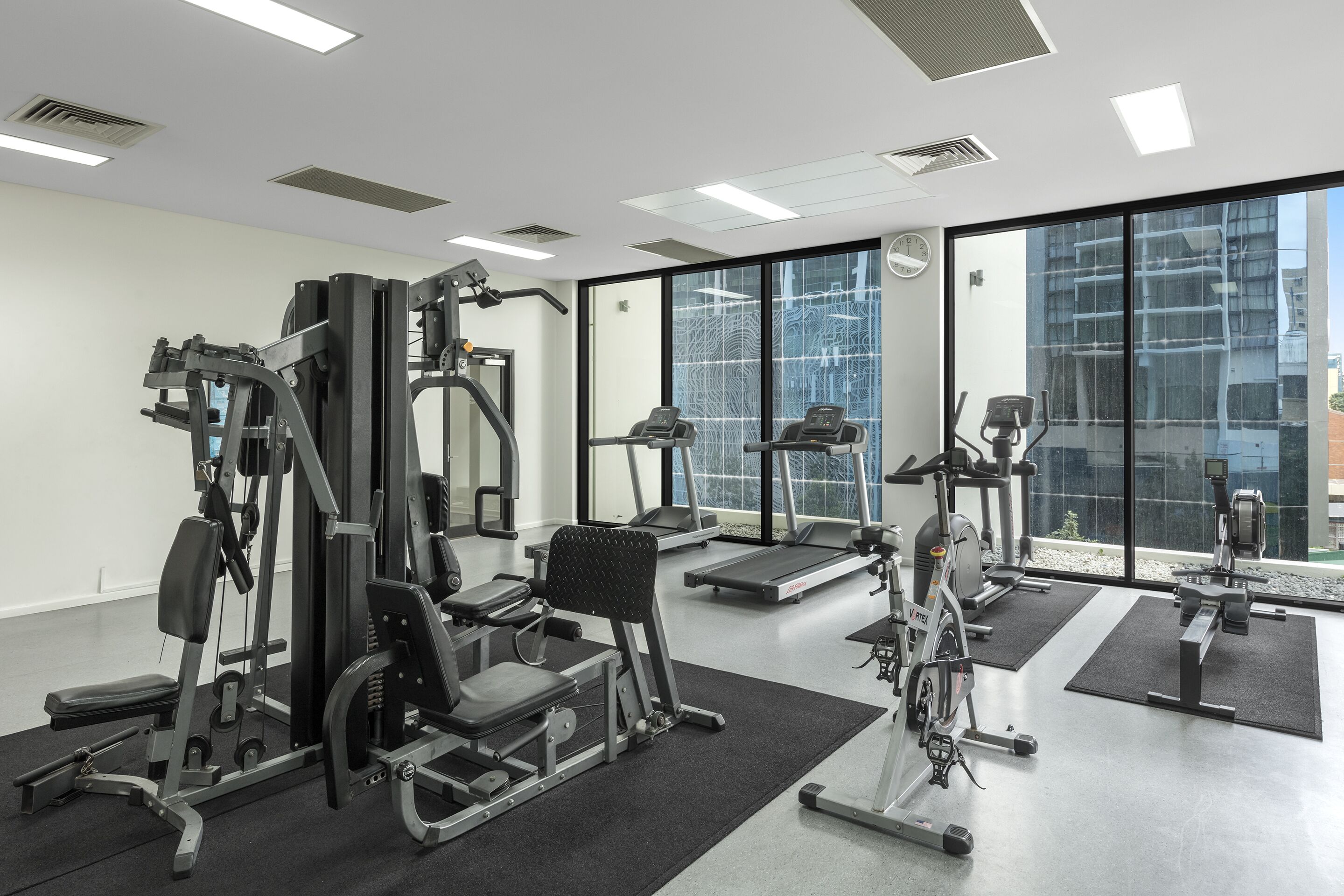 Uma academia moderna com diversos equipamentos de exercício, janelas amplas e um layout espaçoso e limpo.