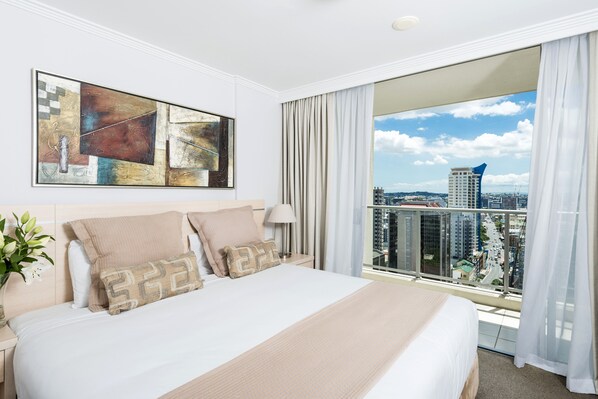 Een hotelkamer met een groot bed, uitzicht op de stad en abstracte kunst aan de muur.