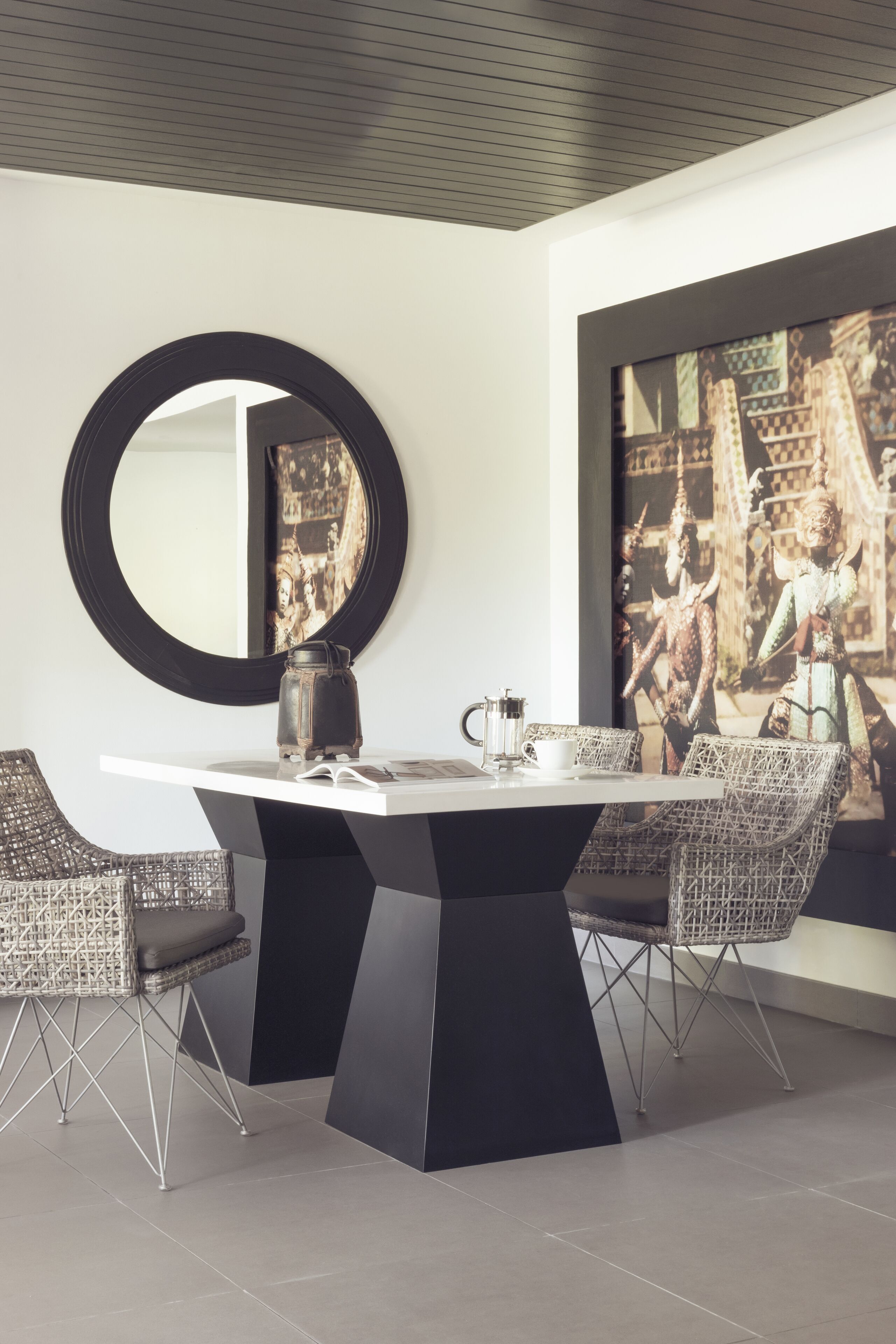 A modern dining area with a round mirror, a white table, and wicker chairs.