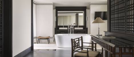A modern bathroom with a bathtub, a vanity with a mirror, and a seating area with chairs.