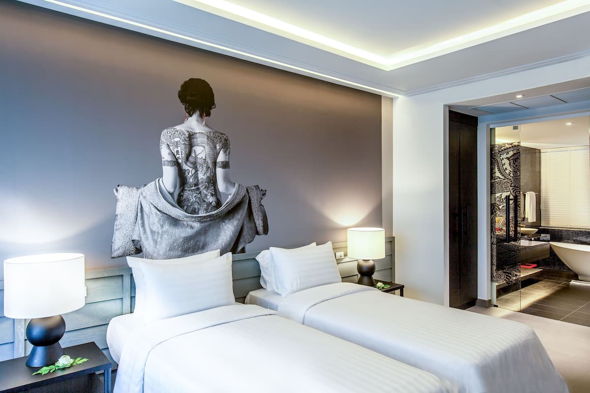 Habitación de hotel con dos camas, una escultura en la pared, baño con bañera y un espejo grande.