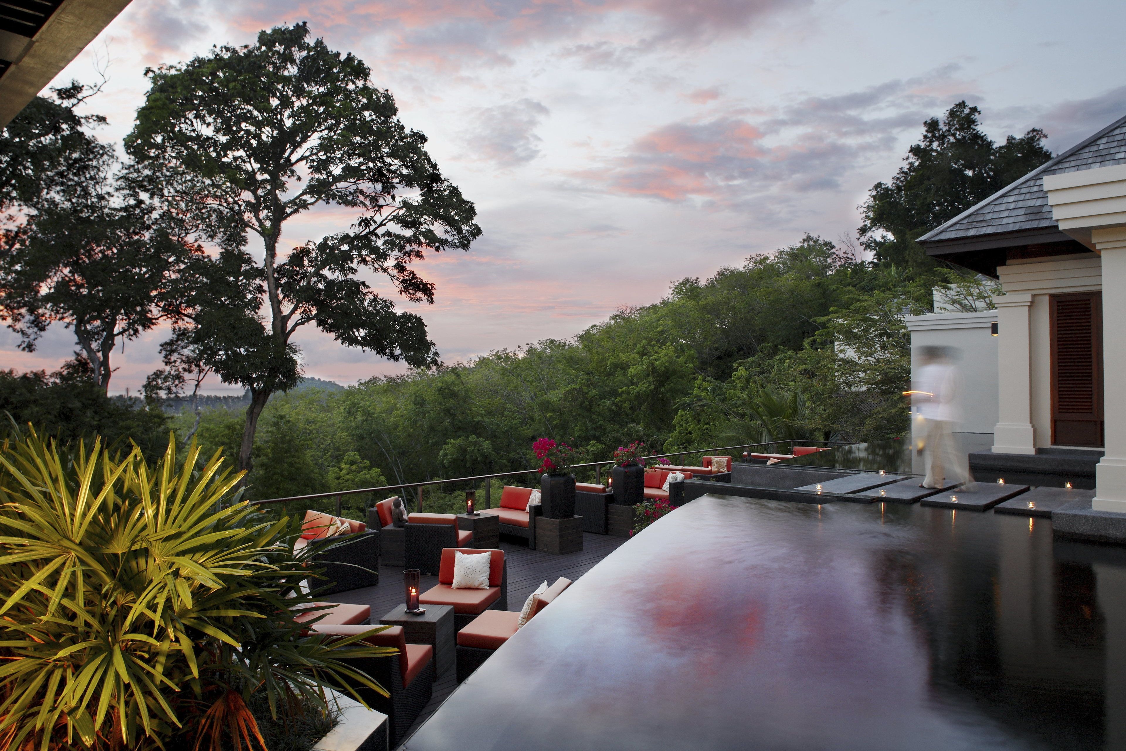 A rooftop bar with outdoor seating, surrounded by lush greenery and trees.
